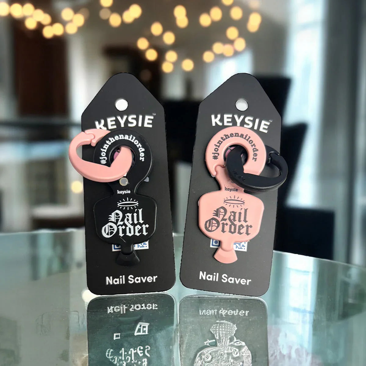 Two Keysie nail saver keyring openers on display, one black and one pink, with branded packaging.