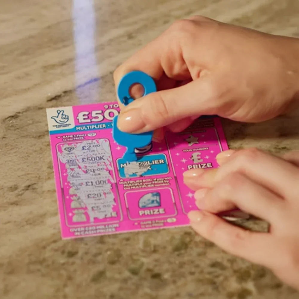Hand using blue keyring tool to scratch off lottery ticket on tabletop
